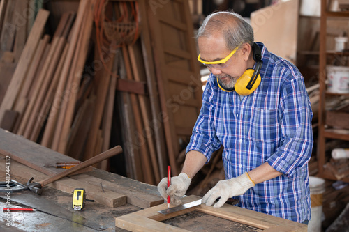 senior man carpenter measuring wood with ruler in workshop