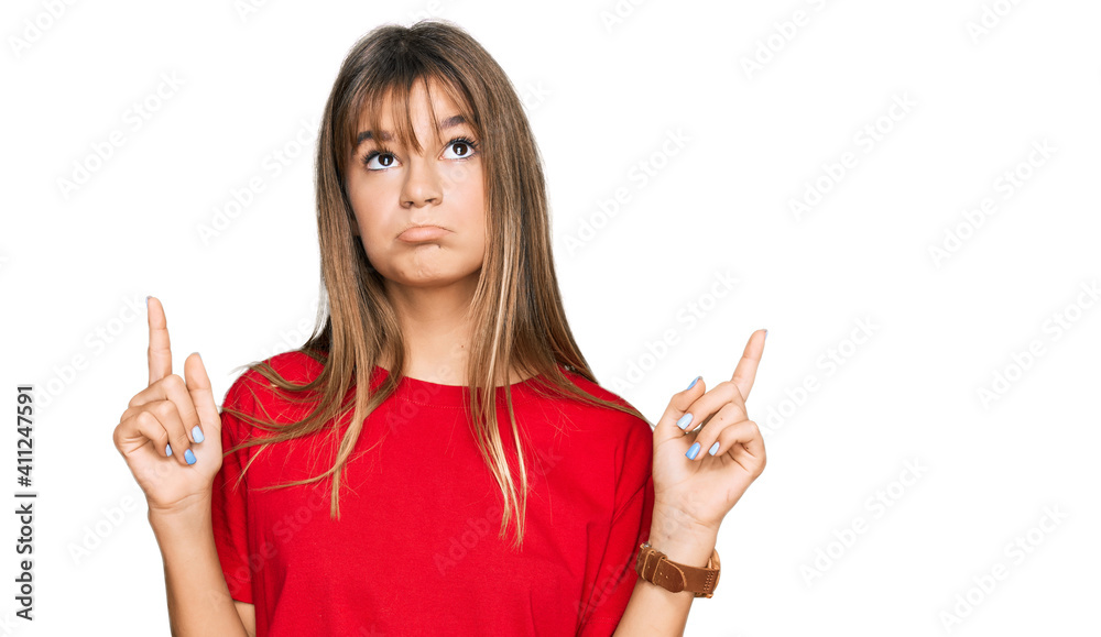 Teenager caucasian girl wearing casual red t shirt pointing up looking sad and upset, indicating direction with fingers, unhappy and depressed. Teenager caucasian girl wearing casual red t shirt pointing up looking sad and upset, indicating direction with fingers, unhappy and depressed.