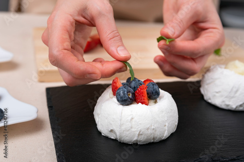 Womens hands decorate cake. Fresh berries and white meringue.