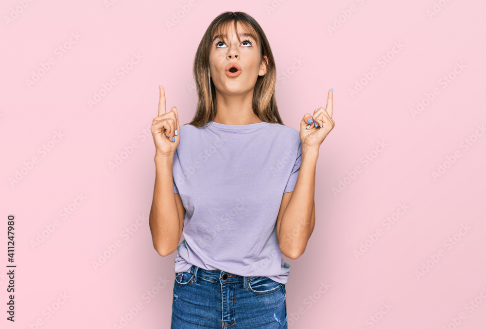 Teenager caucasian girl wearing casual clothes amazed and surprised looking up and pointing with fingers and raised arms. Teenager caucasian girl wearing casual clothes amazed and surprised looking up and pointing with fingers and raised arms.