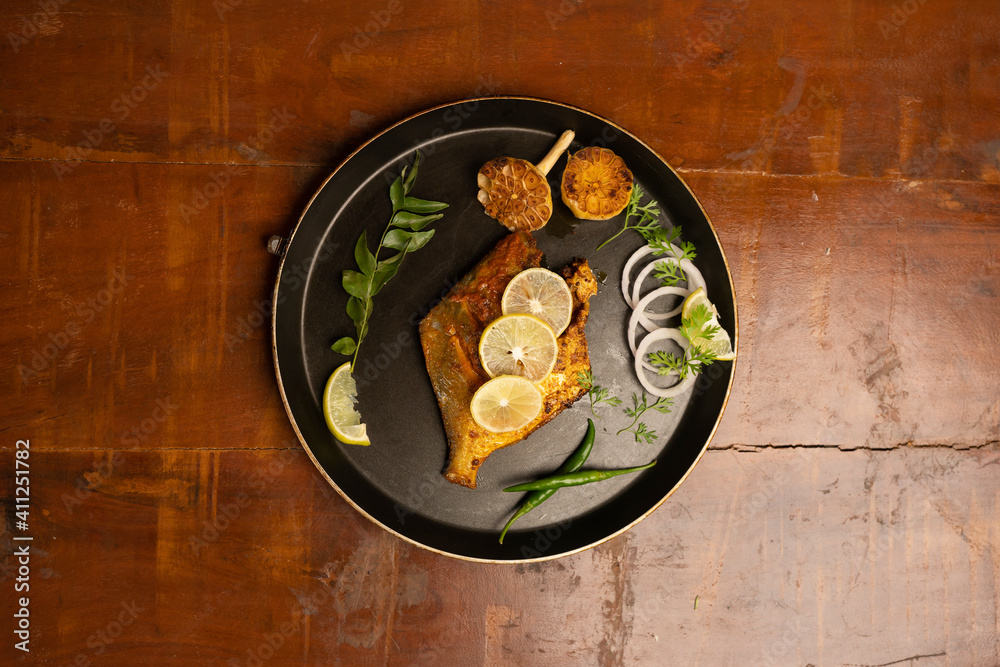 pomfret fish fry- deeply fried two pomfret fishes which is well garnished with lemon and onion in a white ceramic plate with wooden background pomfret fish fry- deeply fried two pomfret fishes which is well garnished with lemon and onion in a white ceramic plate with wooden background