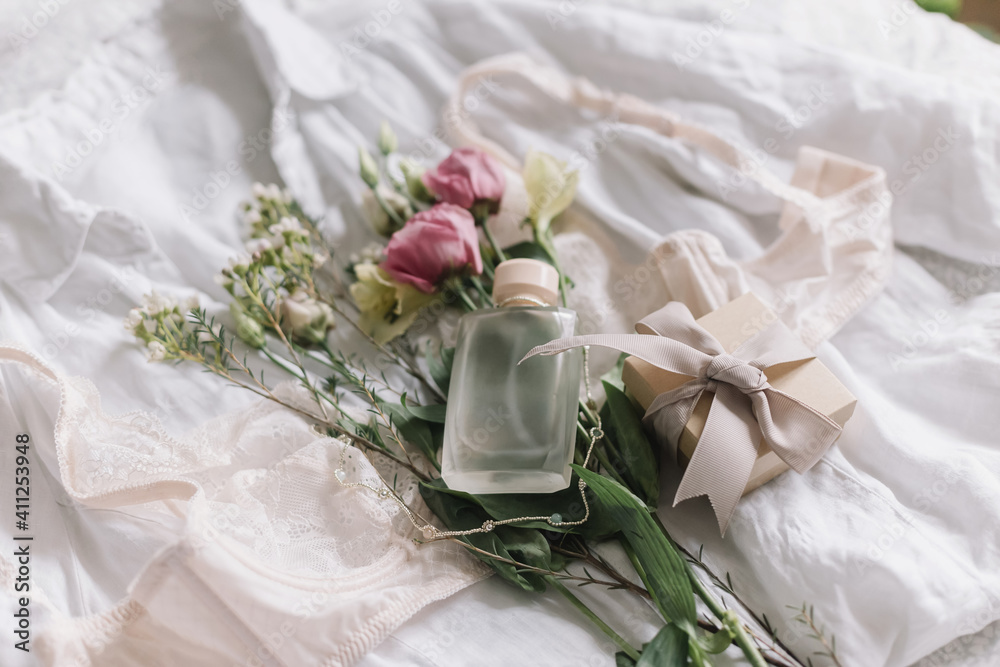 Fototapeta premium Stylish lingerie, gift, jewelry, perfume bottle and spring flowers on bed. Soft trendy image