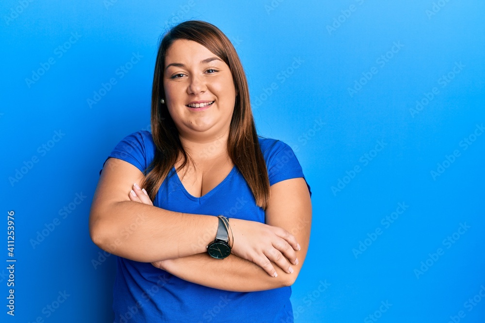 Beautiful brunette plus size woman wearing casual blue t shirt happy face smiling with crossed arms looking at the camera. positive person. Beautiful brunette plus size woman wearing casual blue t shirt happy face smiling with crossed arms looking at the camera. positive person.