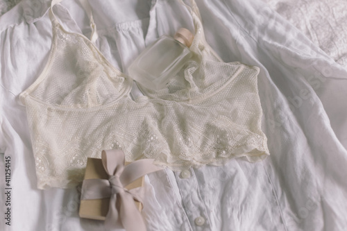 Stylish lace lingerie, gift box, perfume bottle on bed. Soft trendy image. Women's day