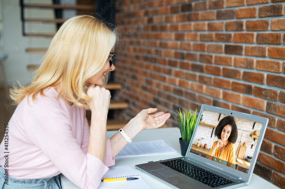 Video call concept. Two female colleagues speak online via video connection on the laptop. A middle-aged teacher has virtual conference with a student - obrazy, fototapety, plakaty 