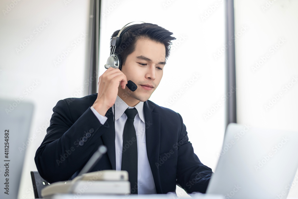 Young Asian man wearing headphones are serving customers With a laptop at the office. Young Asian man wearing headphones are serving customers With a laptop at the office.