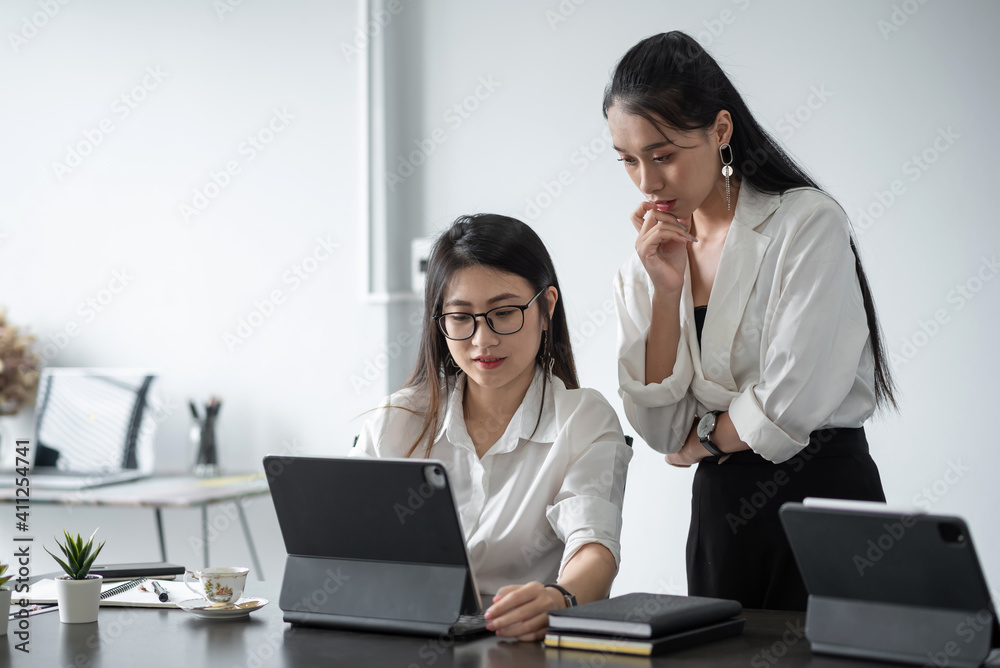 Two beautiful Asian businesswoman share corporate experiences and consult work using a digital tablet at the office Two beautiful Asian businesswoman share corporate experiences and consult work using a digital tablet at the office