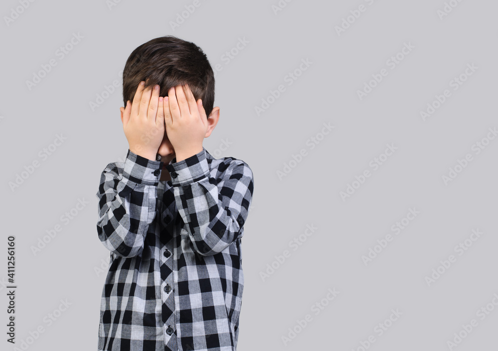 Unhappy schoolboy, 6-year-old boy covered his face with his hands on studio gray isolated background.Resentful boy Unhappy schoolboy, 6-year-old boy covered his face with his hands on studio gray isolated background.Resentful boy