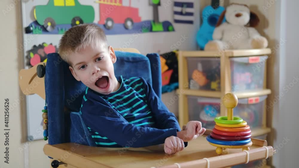 Sensory Activities for kids with disabilities. Preschool Activities for Children with Special Needs. Boy with with Cerebral Palsy in special chair play and smile at home.