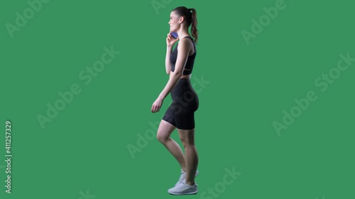 Side view of happy sporty fit woman walking and talking on the cell phone. Full body on chroma key green screen.