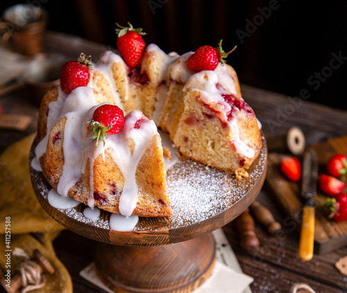tasty homemade bundt cake with strawberries and white glaze on top on wooden cake stand on rustic table