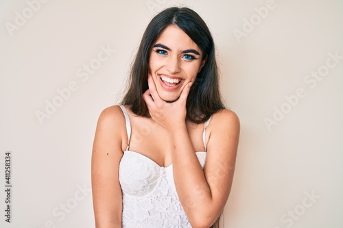 Brunette teenager girl posing elegant looking confident at the camera smiling with crossed arms and hand raised on chin. thinking positive.