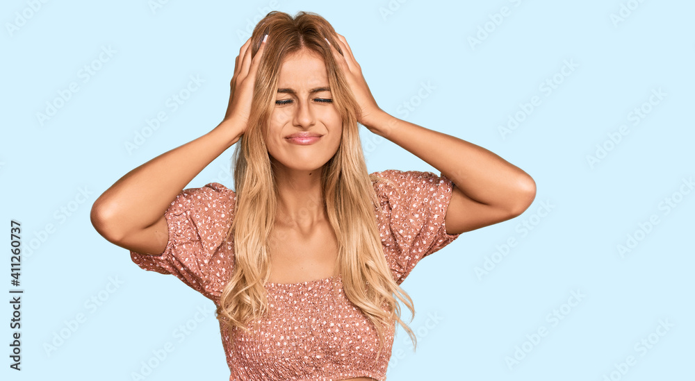 Beautiful blonde young woman wearing summer top suffering from headache desperate and stressed because pain and migraine. hands on head. Beautiful blonde young woman wearing summer top suffering from headache desperate and stressed because pain and migraine. hands on head.