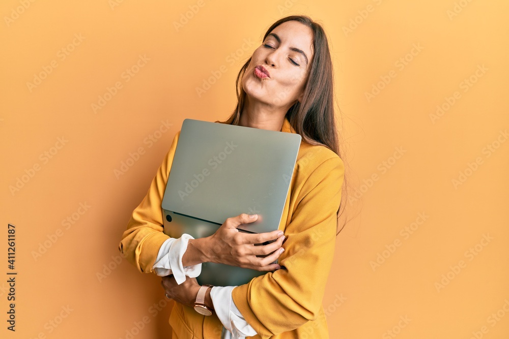 Fototapeta premium Young beautiful woman holding laptop looking at the camera blowing a kiss being lovely and sexy. love expression.