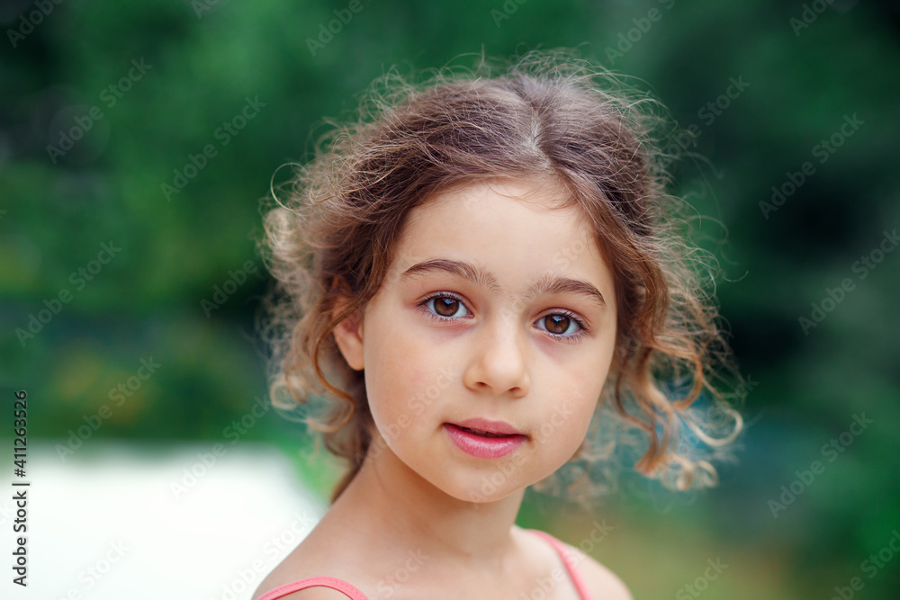 Portrait of smiling beautiful little girl at green of summer park. Happy kid looking at the camera Portrait of smiling beautiful little girl at green of summer park. Happy kid looking at the camera