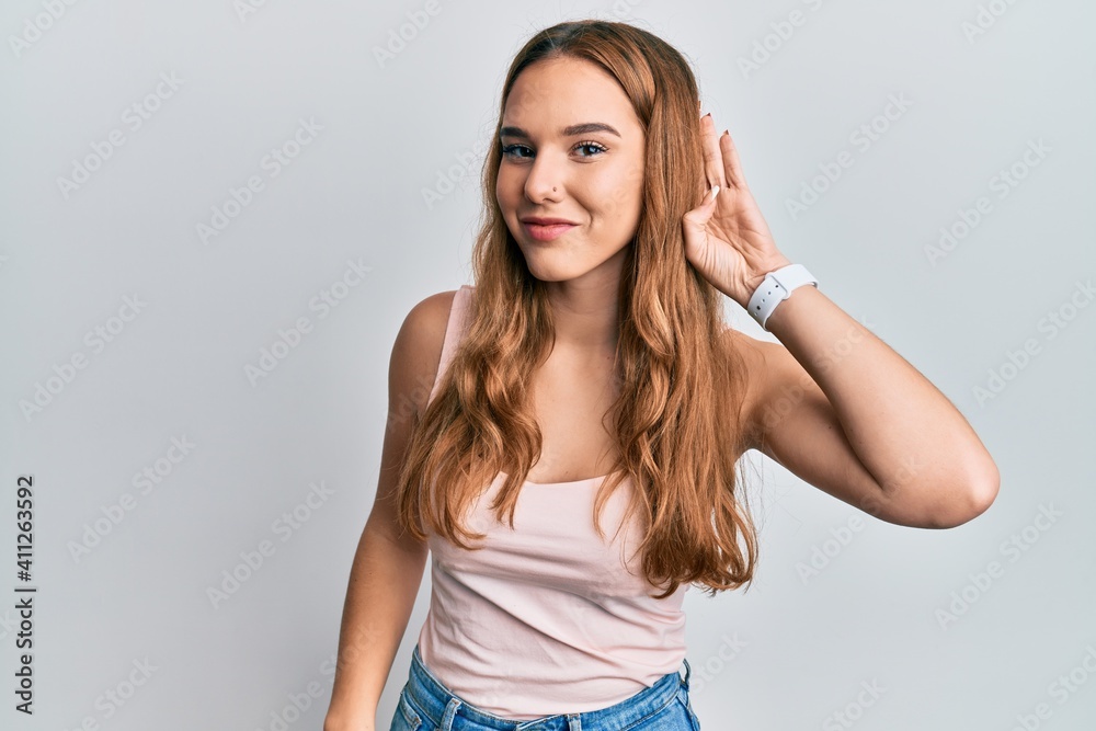 Young blonde woman wearing casual style with sleeveless shirt smiling with hand over ear listening and hearing to rumor or gossip. deafness concept.