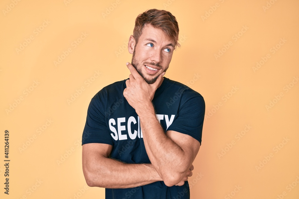 Young caucasian man wearing security t shirt with hand on chin thinking about question, pensive expression. smiling with thoughtful face. doubt concept. Young caucasian man wearing security t shirt with hand on chin thinking about question, pensive expression. smiling with thoughtful face. doubt concept.
