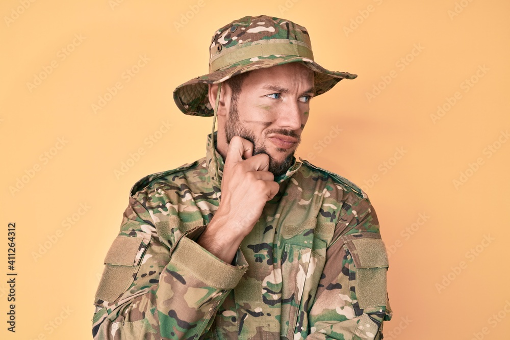 Young caucasian man wearing camouflage army uniform thinking concentrated about doubt with finger on chin and looking up wondering