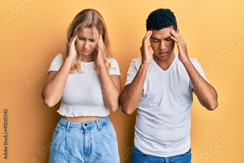 Young interracial couple wearing casual white tshirt with hand on head for pain in head because stress. suffering migraine.