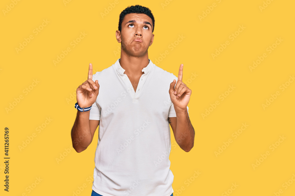 Young arab man wearing casual clothes pointing up looking sad and upset, indicating direction with fingers, unhappy and depressed. Young arab man wearing casual clothes pointing up looking sad and upset, indicating direction with fingers, unhappy and depressed.