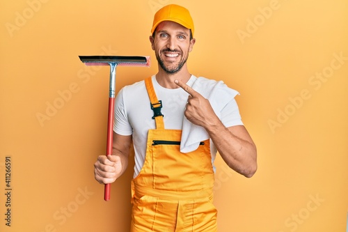 фотографія Young handsome man wearing glass clenaer uniform and squeegee smiling happy poin