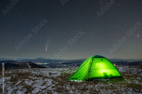 Winter tent in the mountains against the background of stars and comets