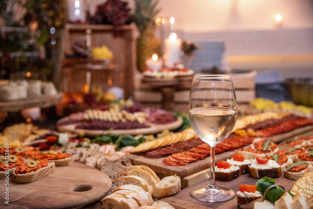 Delicious appertizer catering food with a glass of white wine in center on a wooden table.
