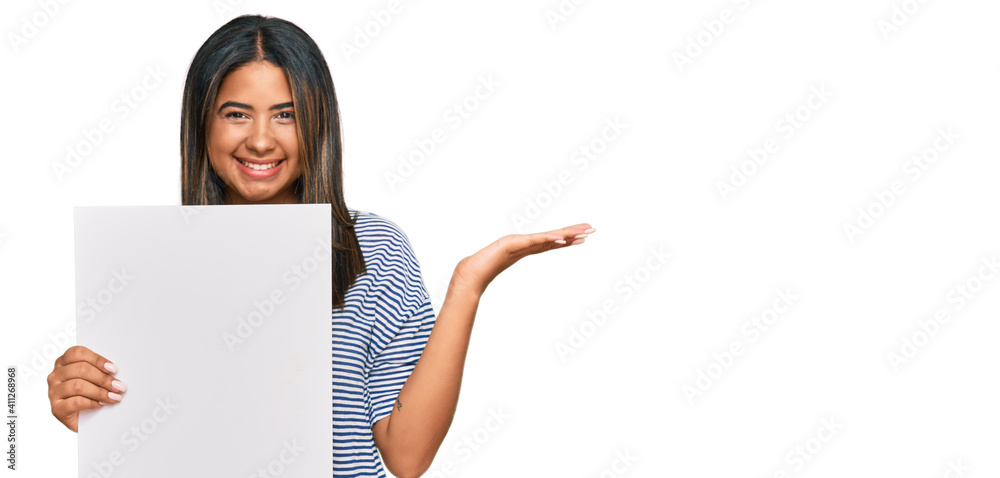 Young latin girl holding blank empty banner celebrating victory with happy smile and winner expression with raised hands Young latin girl holding blank empty banner celebrating victory with happy smile and winner expression with raised hands