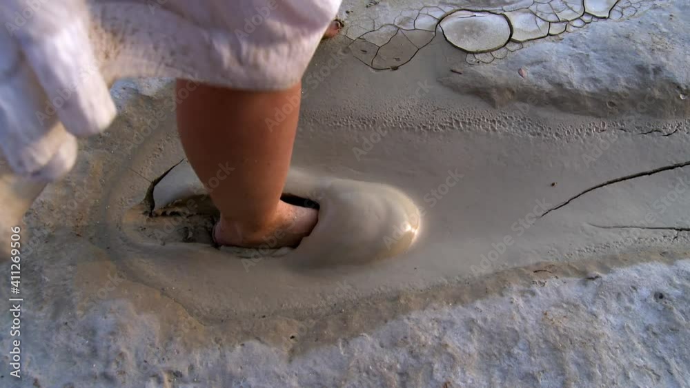 A woman alone in a white dress on a deserted beach walks on a mud path 