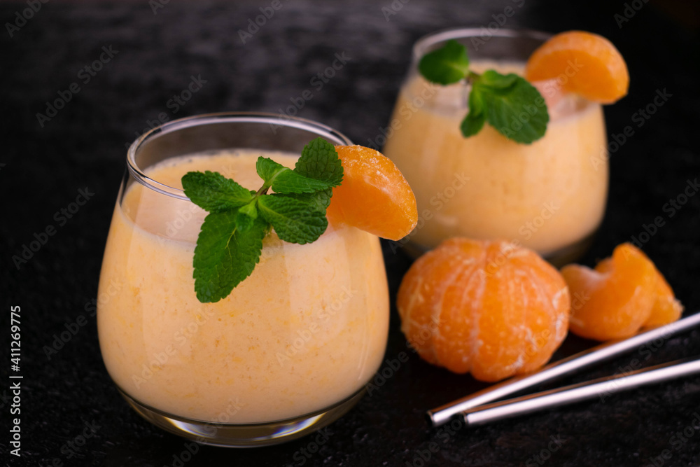 Fototapeta premium Two glasses with delicious tangerine smoothies on a black background.