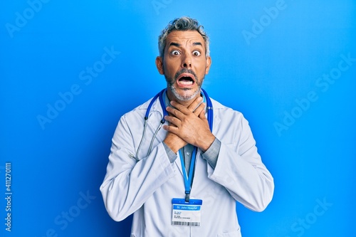 Middle age grey-haired man wearing doctor uniform and stethoscope shouting and suffocate because painful strangle. health problem. asphyxiate and suicide concept.