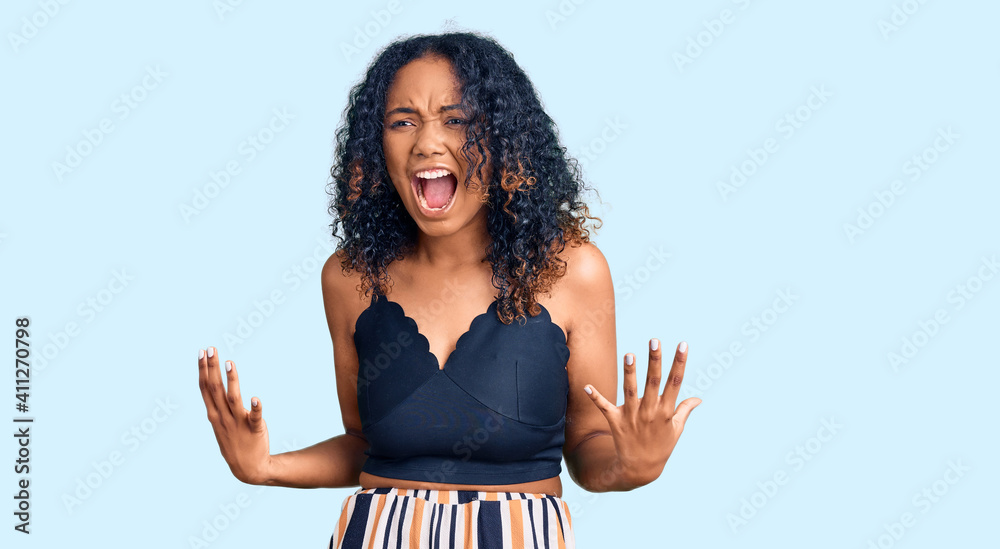 Young african american woman wearing casual clothes crazy and mad shouting and yelling with aggressive expression and arms raised. frustration concept. Young african american woman wearing casual clothes crazy and mad shouting and yelling with aggressive expression and arms raised. frustration concept.