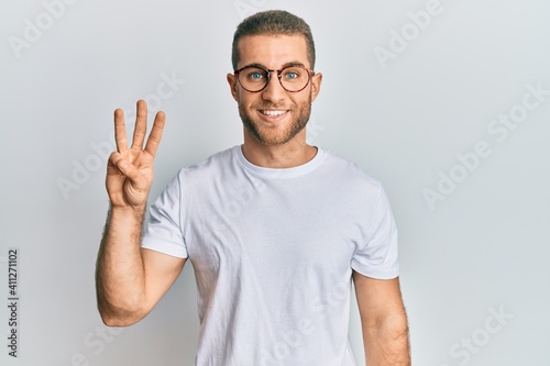 Young caucasian man wearing casual clothes and glasses showing and pointing up with fingers number three while smiling confident and happy. © Krakenimages.com