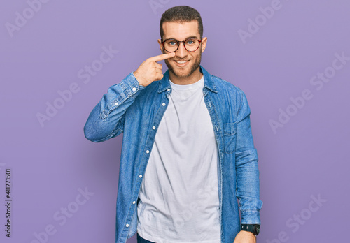 Young caucasian man wearing casual clothes pointing with hand finger to face and nose, smiling cheerful. beauty concept © Krakenimages.com