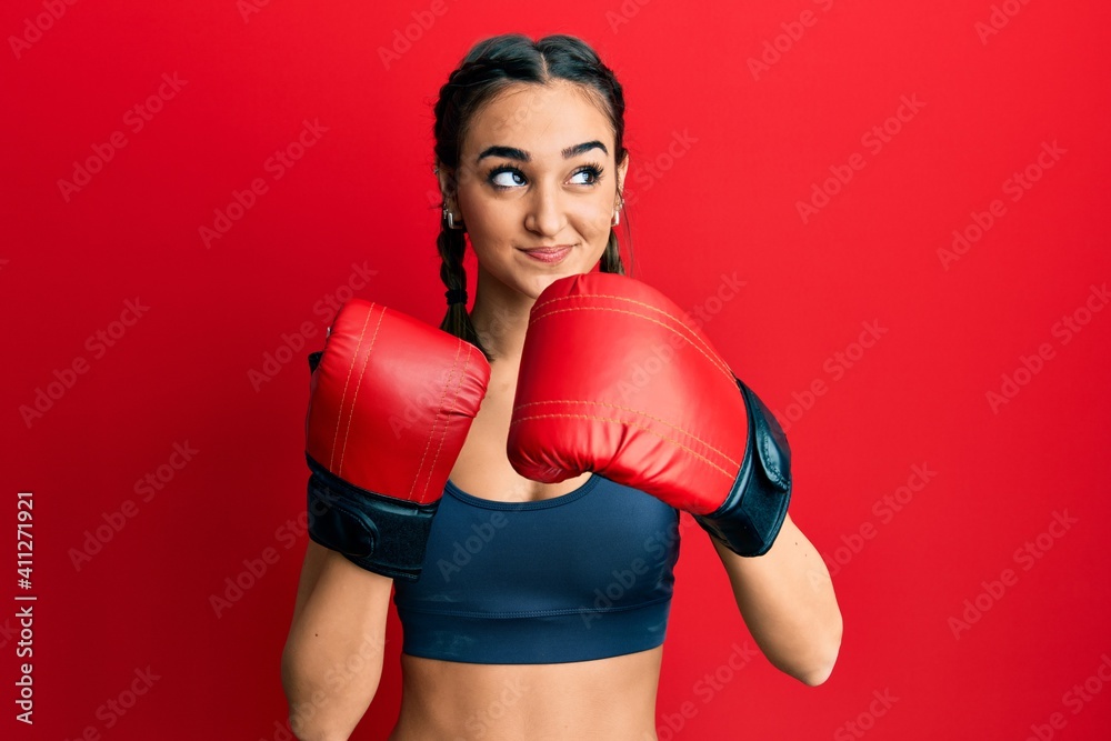Young brunette girl using boxing gloves smiling looking to the side and staring away thinking.