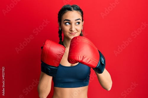 Young brunette girl using boxing gloves smiling looking to the side and staring away thinking. © Krakenimages.com