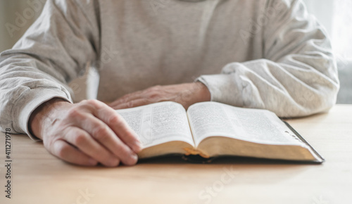 senior man praying, reading an old Bible in his hands.