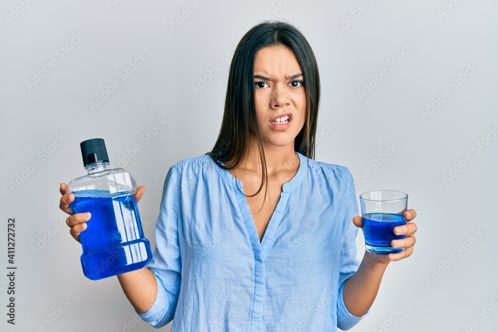 Young hispanic girl holding mouthwash for fresh breath clueless and confused expression. doubt concept. Young hispanic girl holding mouthwash for fresh breath clueless and confused expression. doubt concept.
