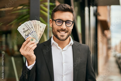 Young hispanic businessman smiling happy holding american dollars at the city.