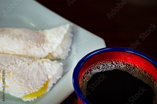 Duas tapiocas recheadas dentro de um prato branco e uma xícara vermelha com café. photo