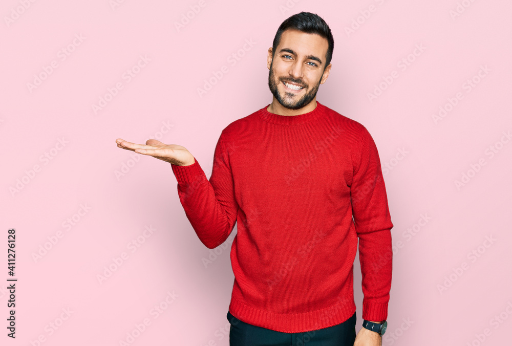 Young hispanic man wearing casual clothes smiling cheerful presenting and pointing with palm of hand looking at the camera. Young hispanic man wearing casual clothes smiling cheerful presenting and pointing with palm of hand looking at the camera.