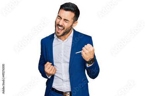 Young hispanic man wearing business jacket celebrating surprised and amazed for success with arms raised and eyes closed. winner concept.