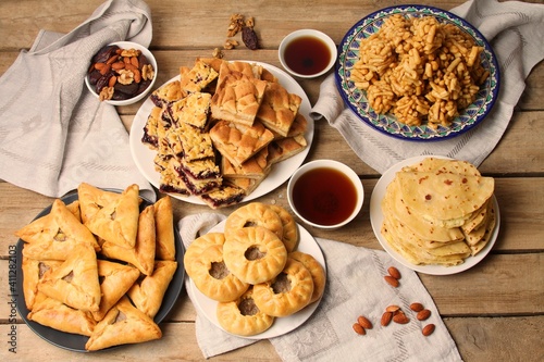 Traditional Tatar Cuisine. Chak chak, Kystybyi, Peremech, Echpochmak, Sweet Belesh With Tea In Original Cup Piala On Wooden Table With Napkins. Flat Lay, Top View.