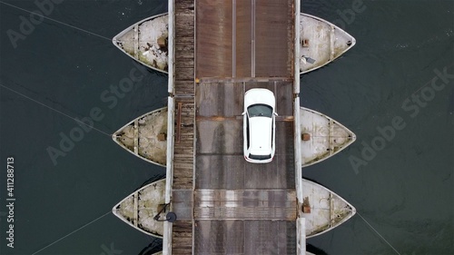 Europe, Italy , Bereguardo  February 2021 - Drone view of danger wooden bridge resting on boats  on Ticino natural park ( Ponte delle barche chiatte ) near Pavia - Cars and people  cross the river  