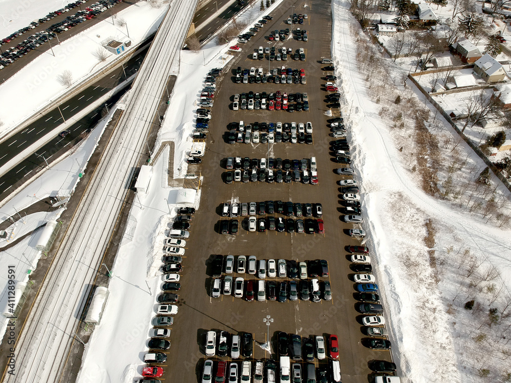 Fototapeta Parking lot filled with cars near commuter train transit at winter. Aerial view. The parking is jammed with cars in winter time. Citizens leaving there cars to travel on train to the city.