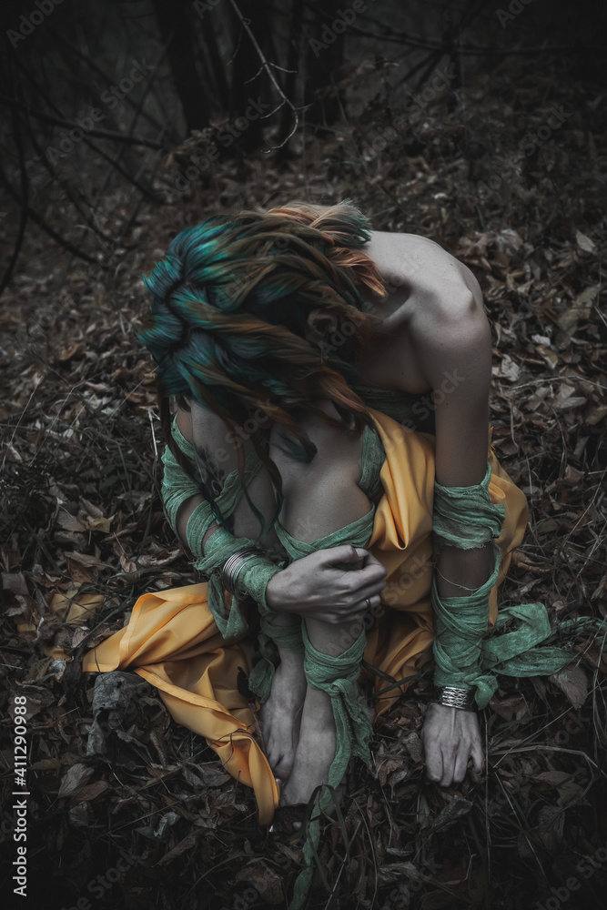 dead girl in autumn foliage wearing green and yellow robes