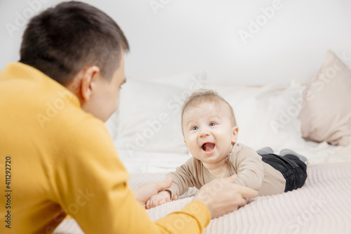 Young father is playing with newborn baby on bed