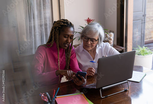 Young African woman teaching an older woman how to use a mobile phone indoors