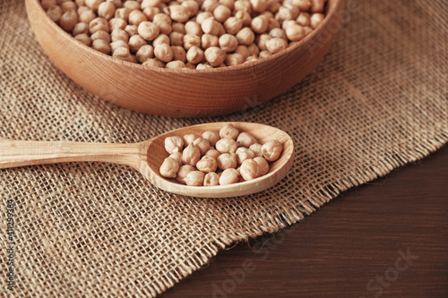 Dry chickpeas in a wooden plate and spoon on a brown wooden background. Copy, empty space for text