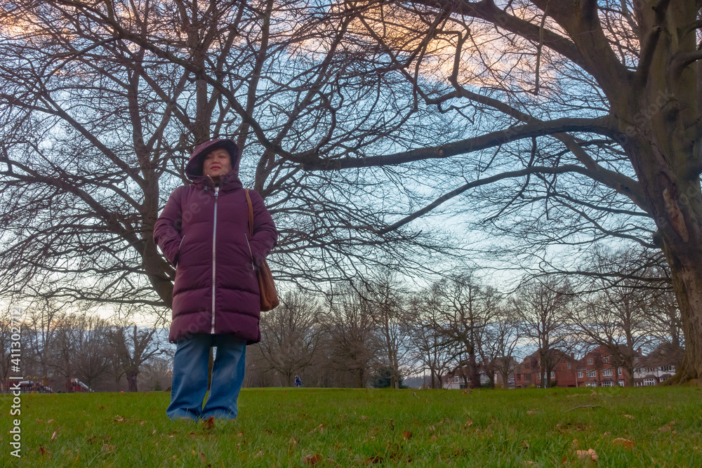 A lady wearing a warm coat, stood in the park shot from a low angle.